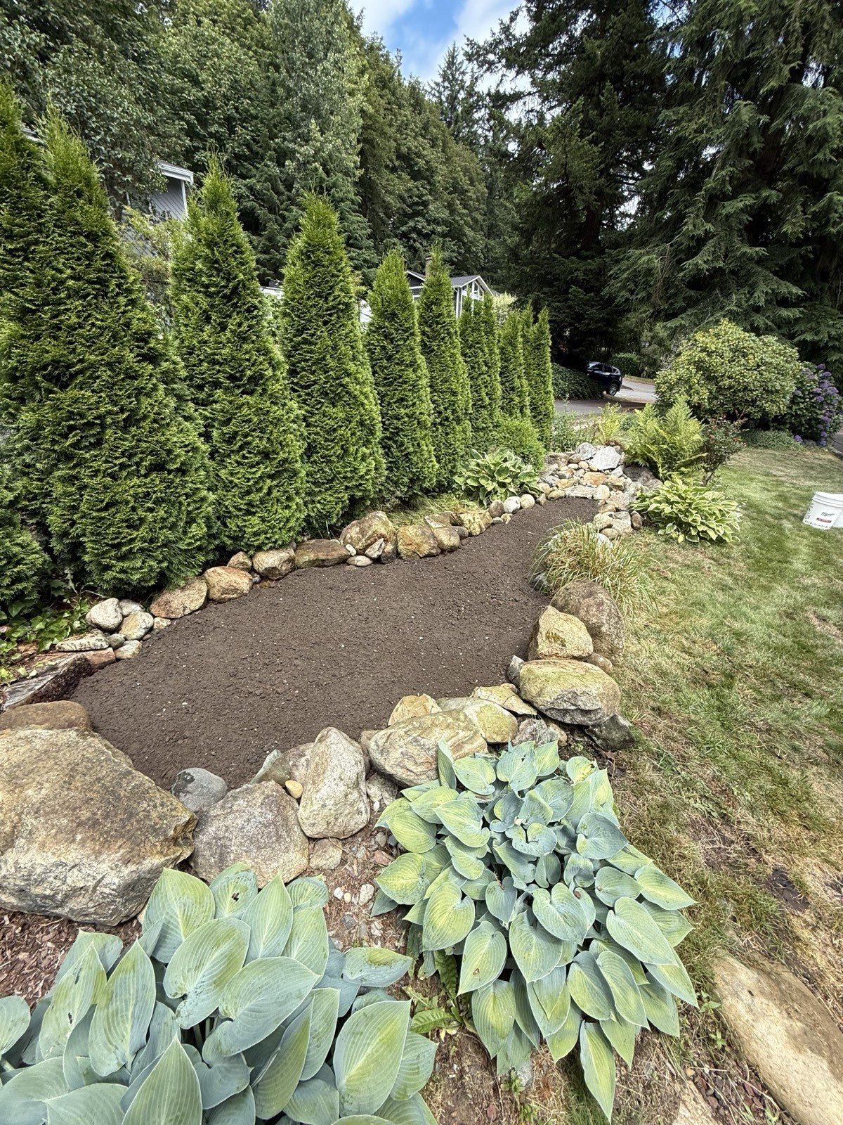 River-rock lined mulch path through a hosta and shrub bed