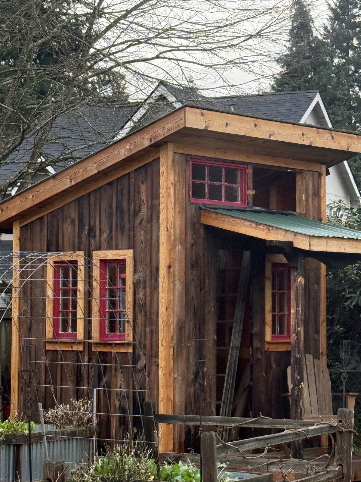 Custom cedar outbuilding with red-trimmed windows and covered entry